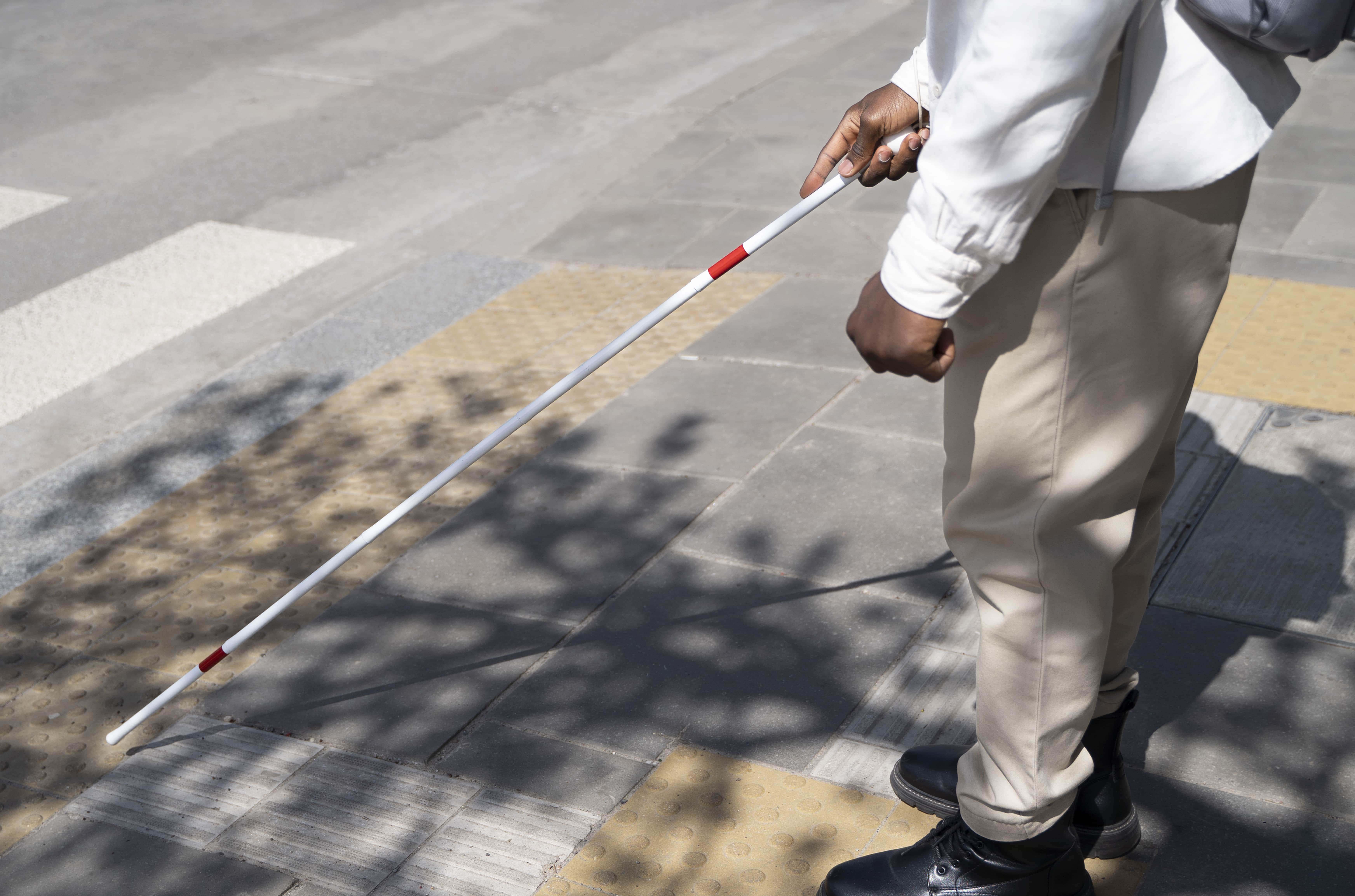Tunanetra Seorang pria yang membawa tongkat tunanetra sedang berjalan di atas guiding block